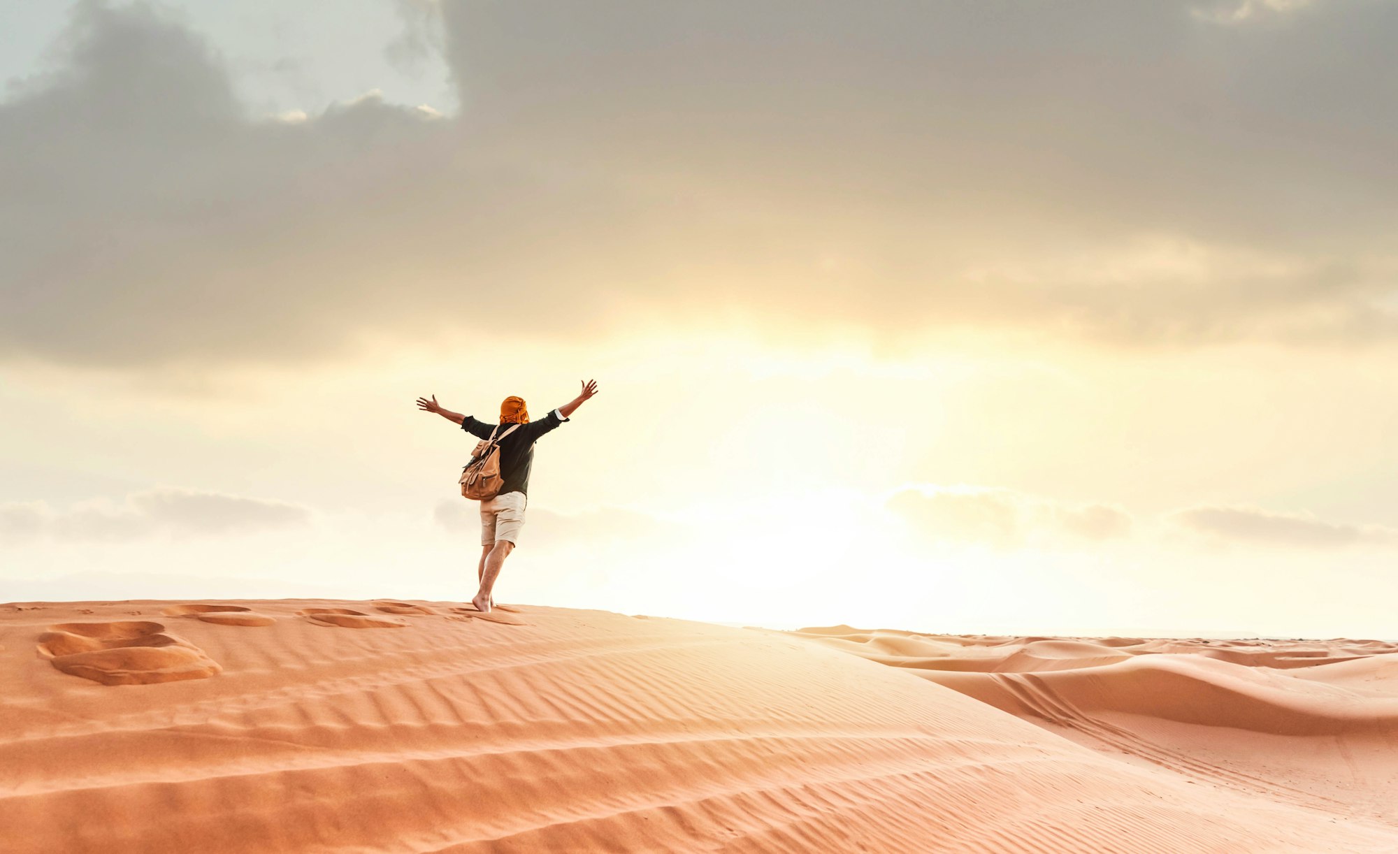 Hiker man walking in the desert sand dunes at sunset